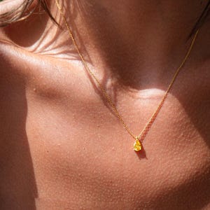 May include: A gold chain necklace with a small, teardrop-shaped pendant. The pendant is a light yellow color.