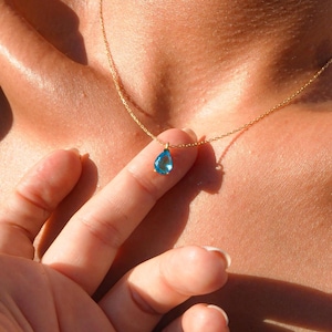 May include: A gold chain necklace with a teardrop-shaped blue gemstone pendant.