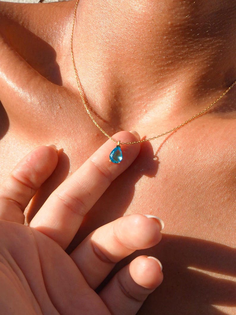 May include: A gold chain necklace with a teardrop-shaped blue gemstone pendant.
