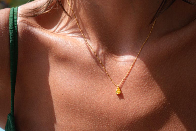 Pode incluir: Um colar de corrente de ouro com um pequeno pingente em forma de l&aacute;grima. O pingente &eacute; de cor amarelo claro.