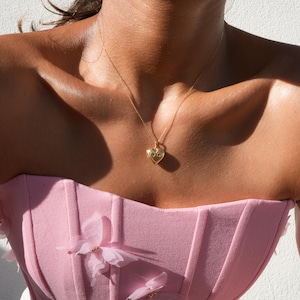 May include: A woman wearing a pink strapless top with floral embellishments and a gold heart pendant necklace.