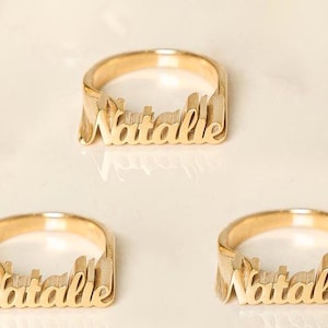 May include: Three gold rings with the name "Natalie" spelled out in cursive lettering.