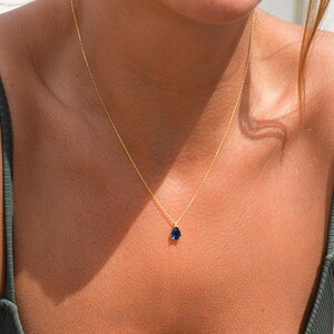 Pode incluir: Um colar de corrente de ouro com um pingente de pedra preciosa azul em forma de l&aacute;grima.