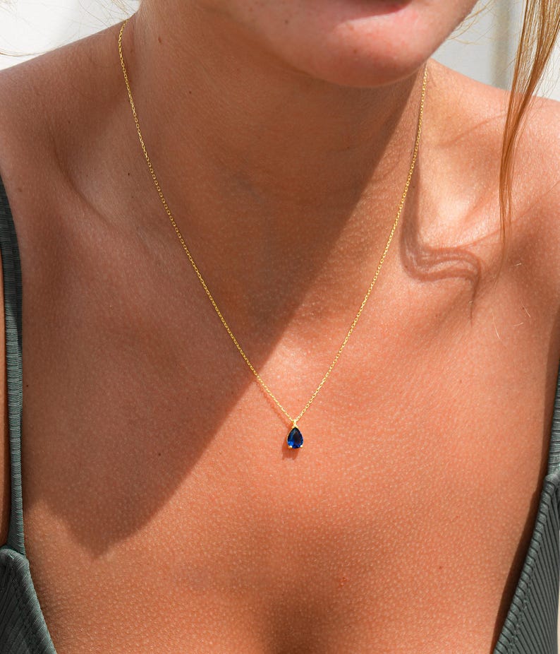 Pode incluir: Um colar de corrente de ouro com um pingente de pedra preciosa azul em forma de l&aacute;grima.