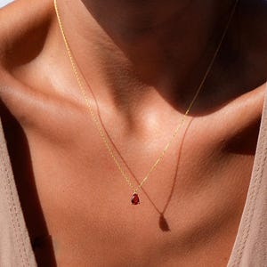 May include: A gold chain necklace with a small, teardrop-shaped red gemstone pendant.