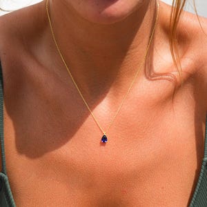 May include: A gold chain necklace with a small teardrop-shaped blue gemstone pendant.