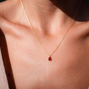 May include: A gold chain necklace with a small, teardrop-shaped red gemstone pendant.