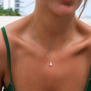 Peut inclure: Un collier en chaîne dorée avec un pendentif en forme de larme orné d'une pierre précieuse transparente.