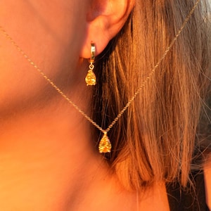 May include: A gold necklace and earrings with a teardrop-shaped pendant set with a yellow gemstone.