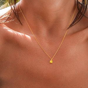May include: A gold chain necklace with a small, textured, gold pendant. The necklace is worn by a person with tanned skin.