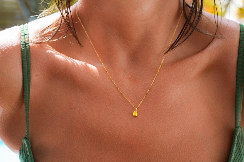 May include: A gold chain necklace with a small, textured, gold pendant. The necklace is worn by a person with tanned skin.