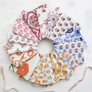 May include: A circular arrangement of folded fabric squares with floral patterns in various colors, including pink, orange, blue, and yellow. The fabrics are arranged in a circle, showcasing a variety of designs. Ribbons with the word "FABLEISM" are visible.