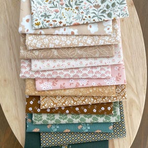 May include: A stack of folded fabric squares featuring a variety of patterns including floral prints, geometric shapes, and botanical motifs in a color palette of cream, beige, soft pink, mustard yellow, sage green, and deep forest green.
