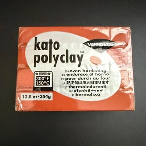 May include: A rectangular package of Kato PolyClay in a reddish-orange hue. The package features the brand name in white, along with text indicating it is oven-hardening. It weighs 12.5 oz (354g) and can be baked at 300°F (150°C).