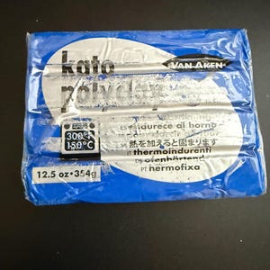 May include: A blue package of Kato Polyclay polymer clay. The package has a white oval with the brand name and product information. The package also includes the weight of the clay, 12.5 oz (354g), and baking instructions.