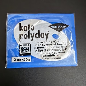 May include: A blue package of Kato PolyClay, a polymer clay product. The package features the brand name and product information, including oven hardening instructions at 300°F (150°C). The package contains 2 oz (56g) of clay.