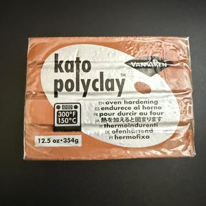 May include: A package of Kato Polyclay in a warm, reddish-brown hue. The packaging features the brand name and product details, including oven-hardening instructions and a weight of 12.5 oz (354g). The clay is designed for oven baking at 300°F (150°C).
