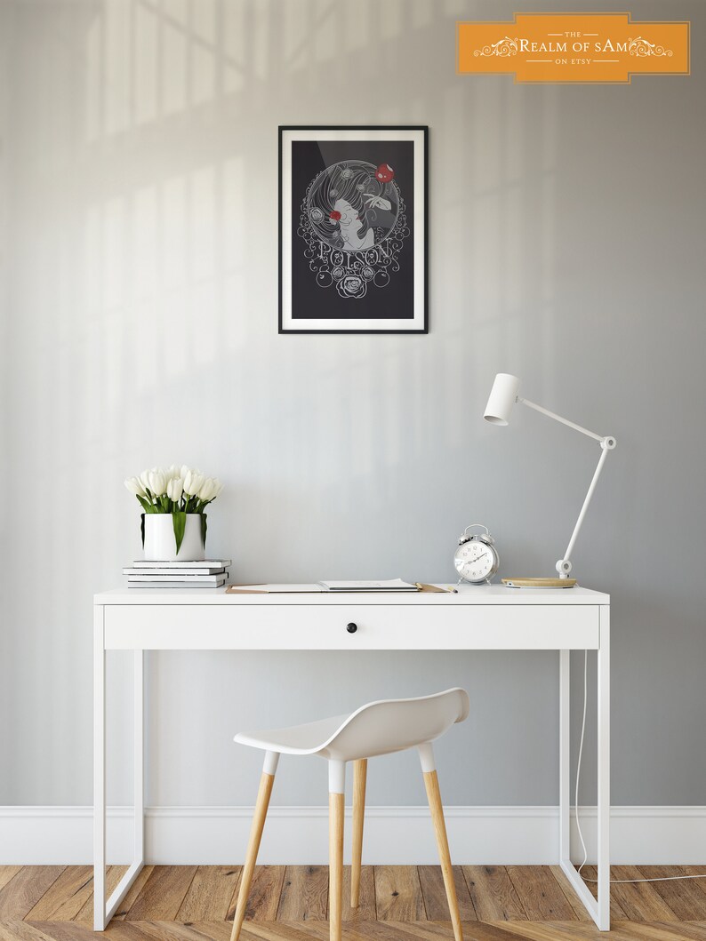 May include: A black and white illustration of a woman with a red apple in her hand. The illustration is surrounded by a circle of roses and the word "Poison" is written in a decorative font. The illustration is framed in black and hanging on a gray wall above a white desk with a white chair.