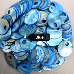 May include: A collection of circular blue shell discs, each featuring a single off-center hole. The discs exhibit a natural iridescent sheen with varying shades of light and dark blue, layered together in a dense, overlapping pile with a black tag.