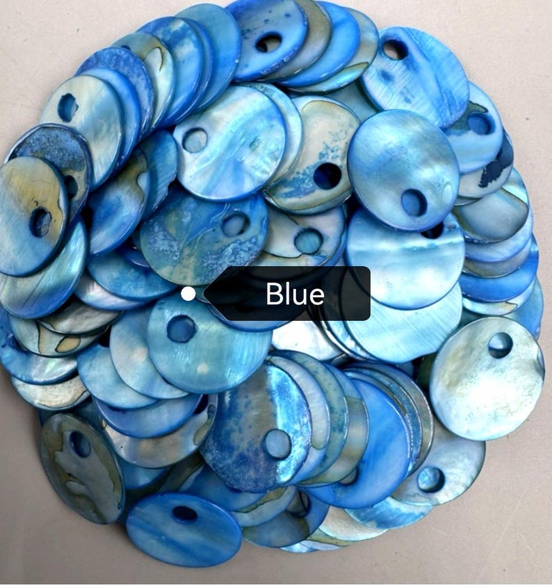 May include: A collection of circular blue shell discs, each featuring a single off-center hole. The discs exhibit a natural iridescent sheen with varying shades of light and dark blue, layered together in a dense, overlapping pile with a black tag.