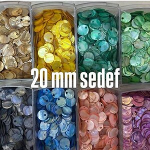 May include: A collection of 20 mm mother of pearl shell discs organized in twelve clear plastic bins. The circular discs feature a single hole and are sorted by color, including blue, gold, yellow, teal, green, orange, olive, grey, pink, purple, and white.