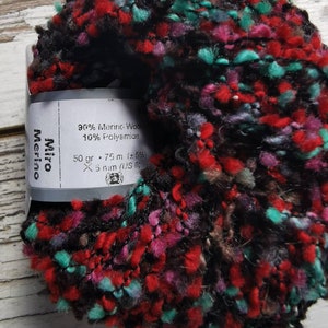 May include: A skein of black, red, pink, and teal yarn with a label that reads "90% Merino Woo 10% Polyamide 50 gr 75 m (±5%) X 5 mm (US 8) Merino Miro".