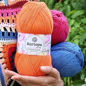 Op de afbeelding: Drie bollen garen in oranje, roze en blauw. De oranje bol heeft een label met de tekst "Karotopu Cotton Love 100 g / 330 m".