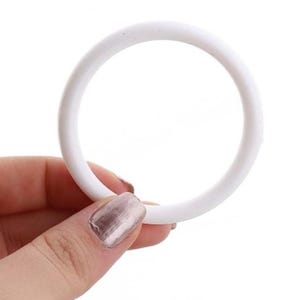 May include: A white, circular object, possibly a ring or a part of a larger item. The object is held by a hand with painted nails. The ring is made of a solid, opaque material and has a smooth surface. The background is plain white.