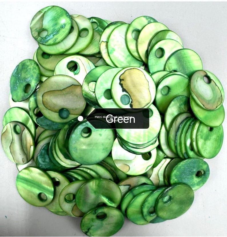 May include: A large collection of circular, flat, green-dyed shell buttons, each featuring a single off-center hole for attachment. The buttons display natural iridescent textures and variations in green tones, with some showing tan patches.