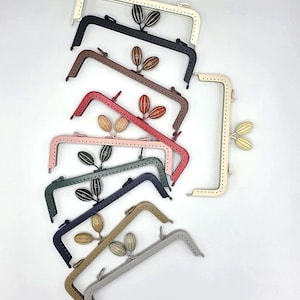 May include: A collection of colourful purse frames in shades such as white, black, brown, pink, green, and grey. Each frame has a decorative leaf-like detail and a rectangular shape. Measurements are in centimetres.