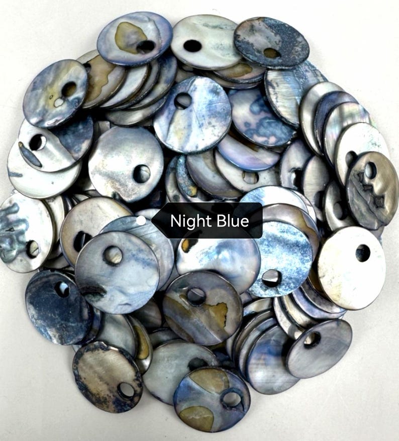 May include: A collection of round, iridescent mother-of-pearl buttons in shades of blue, gray, and silver. Each button features a single off-center hole for attachment. A black rectangular label with the white text Night Blue is visible.