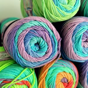 May include: Close-up of several skeins of colorful yarn. The yarn is wound into tight, round balls, showcasing a variety of colors including green, blue, purple, and orange. The yarn appears soft and is likely used for knitting or crocheting projects.