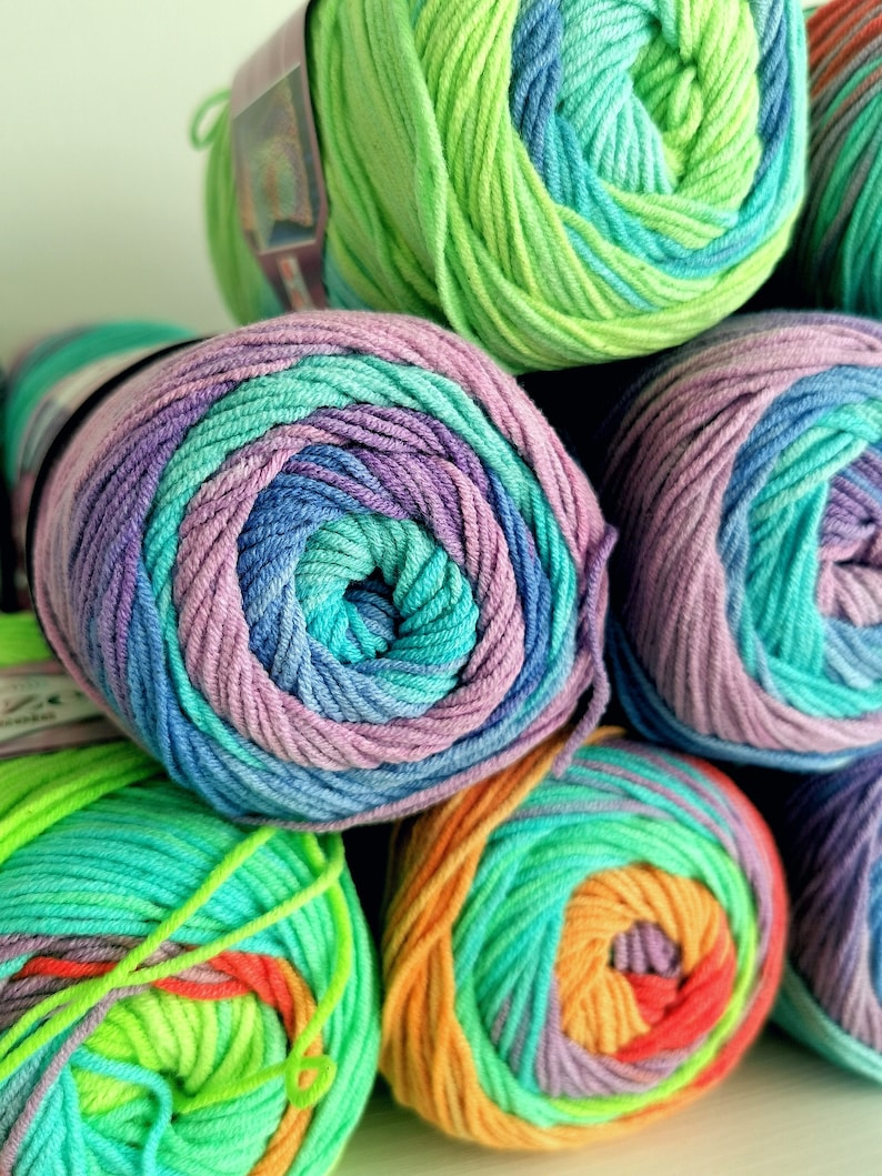 May include: Close-up of several skeins of colorful yarn. The yarn is wound into tight, round balls, showcasing a variety of colors including green, blue, purple, and orange. The yarn appears soft and is likely used for knitting or crocheting projects.