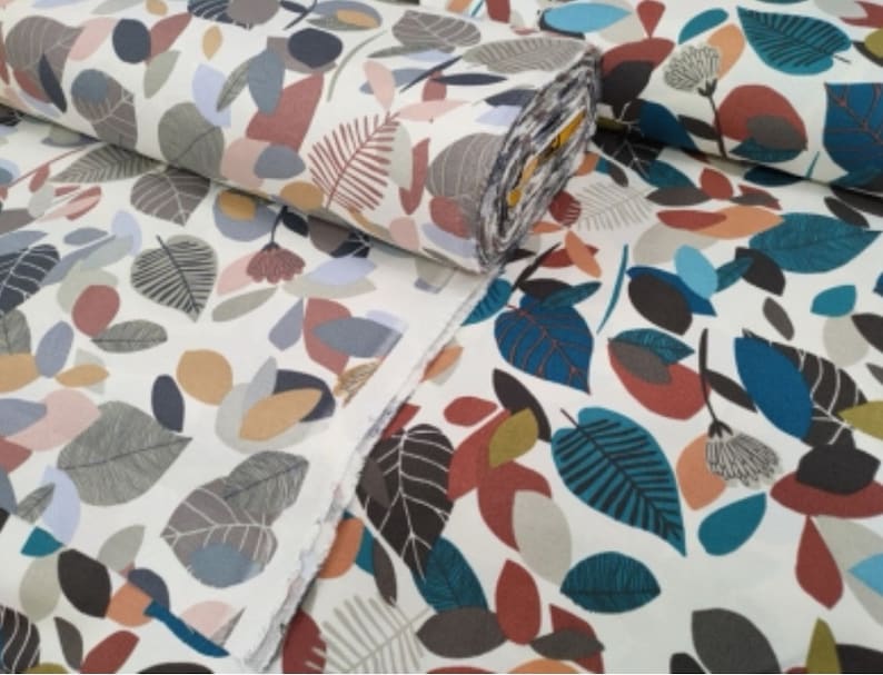 May include: White fabric with a repeating pattern of colorful leaves and abstract shapes. The fabric is folded in half, showing the pattern on both sides.