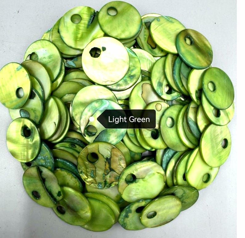 May include: A collection of circular, light green shell discs, each featuring a single off-center hole. The discs exhibit natural variations in tone and texture, with a smooth, iridescent finish. A black label with the text Light Green is visible.