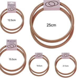 May include: A selection of wooden embroidery hoops in various sizes: 12.5cm, 15.5cm, 18.5cm, 21.5cm, and 25cm. Each hoop is light brown and features a double-ring design. The hoops are packaged with a pink label.