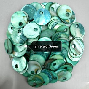 May include: A collection of round, emerald green mother-of-pearl buttons, each featuring a single off-center hole. The buttons display natural iridescent variations and swirling patterns in shades of green, with a black label reading Emerald Green.