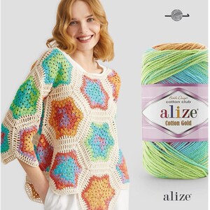 May include: A cream-colored crochet top with colorful hexagon patterns. The top has long sleeves and a round neckline. A skein of Alize Cotton Gold yarn in shades of green, blue, and orange is next to the top.
