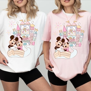 May include: Two white and pink t-shirts with a colorful illustration of Mickey and Minnie Mouse in a boat in front of a castle with the text "It's a Small World".