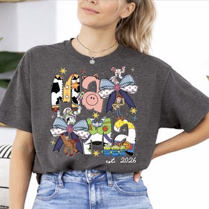 A woman wearing a gray t-shirt with a graphic design featuring various cartoon characters and a date.