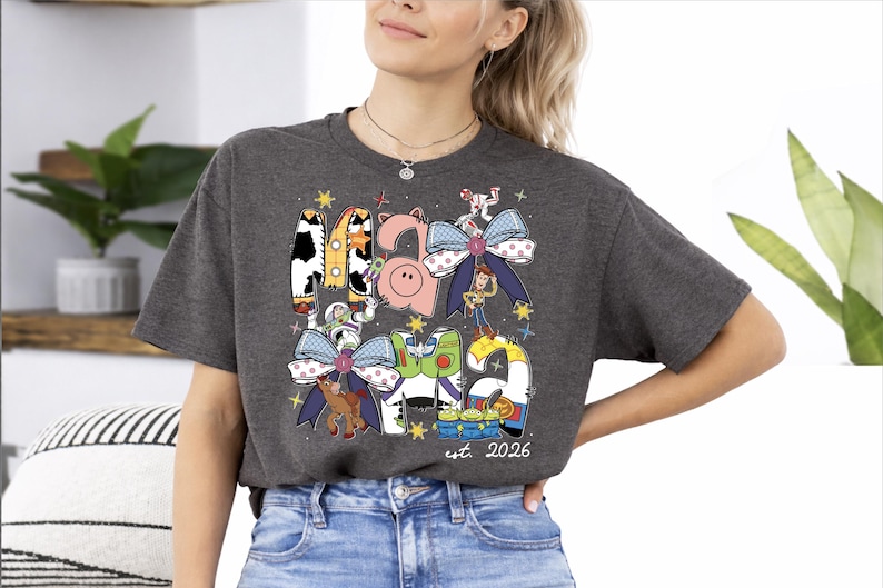 A woman wearing a gray t-shirt with a graphic design featuring various cartoon characters and a date.