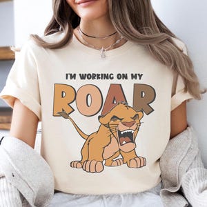 May include: A cream-colored t-shirt with a cartoon lion cub roaring and the text "I'm working on my ROAR".