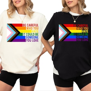 May include: Two t-shirts with a rainbow pride flag and the text "Be careful who you hate. It could be someone you love." The t-shirt on the left is white and the t-shirt on the right is black.