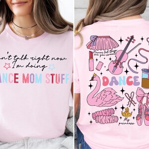 May include: Pink t-shirt with the text "Can't talk right now I'm doing DANCE MOM STUFF" on the front and a pink flamingo, a violin, a ballerina, and other dance-themed illustrations on the back.