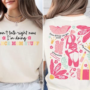 May include: A white t-shirt with the text "Can't talk right now I'm doing DANCE MOM STUFF" on the front. The back of the shirt features a pink and white illustration of dance accessories, including a tutu, ballet shoes, and a crown.