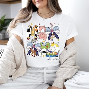 A woman wearing a white t-shirt with a colorful graphic design featuring cartoon characters and text.