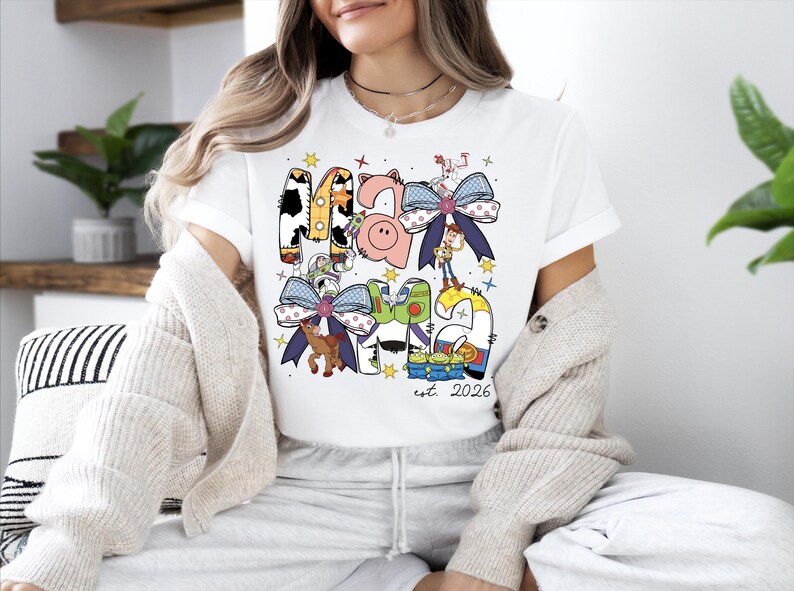 A woman wearing a white t-shirt with a colorful graphic design featuring cartoon characters and text.