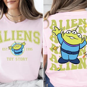 Puede incluir: Camiseta rosa con un personaje extraterrestre verde de Toy Story. La parte delantera de la camiseta dice "ALIENS EST. 1995 TOY STORY". La parte trasera de la camiseta tiene un patr&oacute;n repetido de la palabra "ALIENS" con el personaje extraterrestre en el centro.