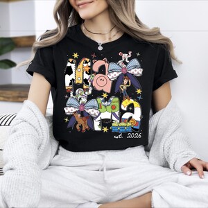 A woman wearing a black t-shirt with a colorful graphic design featuring various cartoon characters and text.
