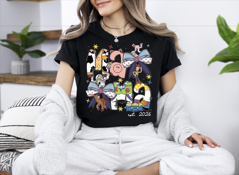 A woman wearing a black t-shirt with a colorful graphic design featuring various cartoon characters and text.